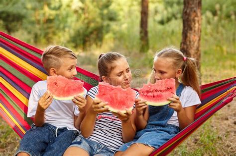 Children Eat Watermelon And Joke Outdoor Sitting On A Colorful