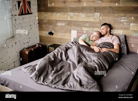 Fröhliche junge schwule Männer sich morgens unter der Decke im Bett entspannen und kuscheln