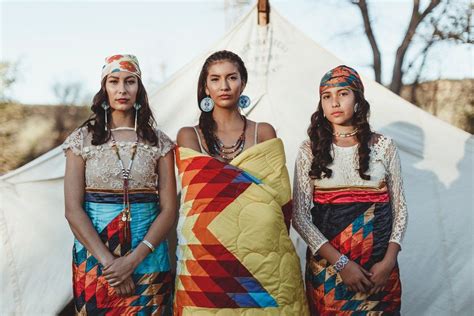 Three Women Standing Next To Each Other In Front Of A Teepee With A