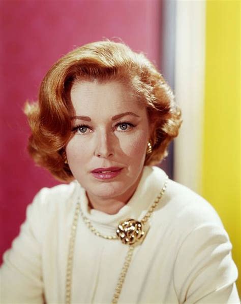 A Woman With Red Hair Wearing A White Sweater And Pearls On Her Neck Is Looking At The Camera