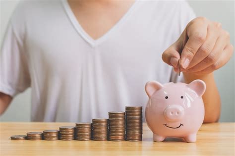 Premium Photo Hand Of Male Putting Coins In Piggy Bank With Money