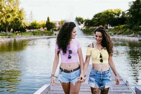 Lesbian Couple Holding Hands While Walking On Pier Against Lake Stock Photo