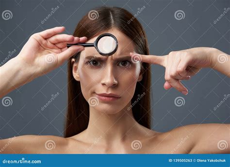 Irritated Young Lady Examining Skin With Magnifying Glass And Frowning
