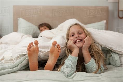 Portrait Of Girl Lying On Bed With Mothers Feet Stock Photo Dissolve