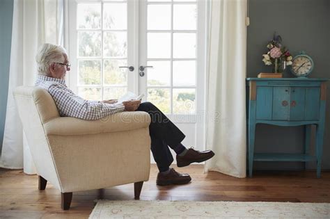 Senior Man Sitting In An Armchair Reading A Book At Home Stock Image