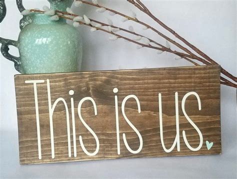 A Wooden Sign That Says This Is Us Next To A Vase With Flowers In It