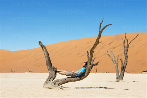 Namibia Namib Desert Man Resting On Dead Tree In Deadvlei Stock Photo