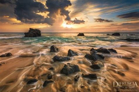 The Sun Is Setting Over The Ocean With Rocks In The Foreground And