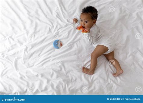 Adorable African American Infant Baby Lying In Bed And Biting Teether