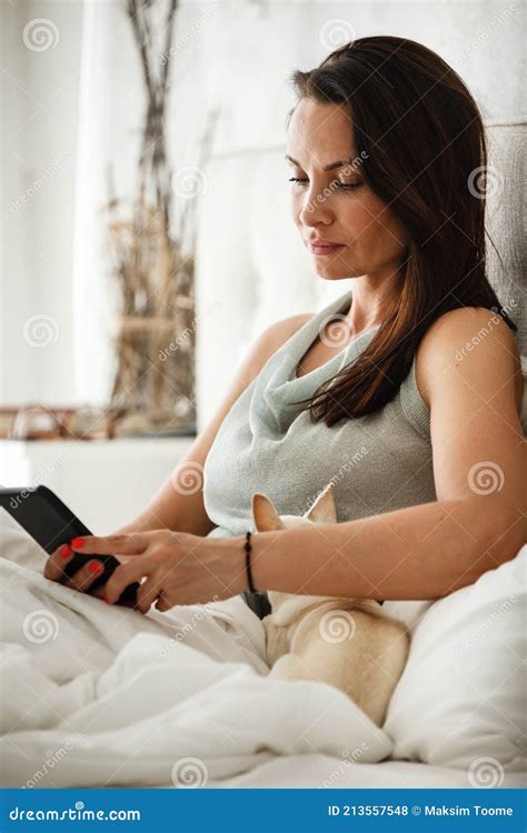 Lazy Morning Concept Beautiful Happy Woman Wakes Up In Bed And Surfes Internet On Phone Stock