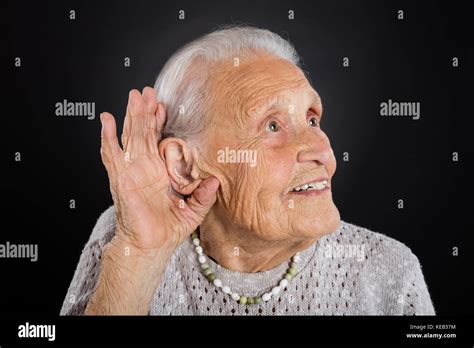 Happy Senior Woman Trying To Hear With Hand Over Ear Over Grey