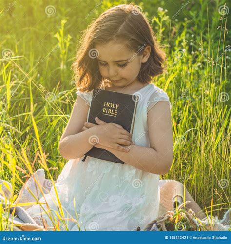 christian girl holds bible in her hands reading the holy bible in a field during beautiful