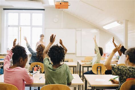 Students Raising Hands While Answering In Classroom At School Stock Photo