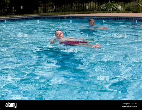Baby Boomer Couple Floating In A Backyard Swimming Pool On A Hot