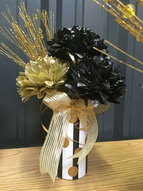 Two Black And White Flowers In A Vase With Gold Ribbons On A Wooden
