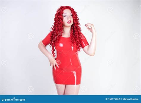 hot sexual redheaded girl with plus size body wears fashion latex rubber red dress and posing on