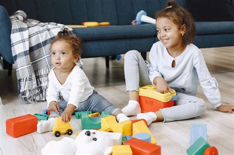 Free Photo Two Pretty Kids Sit On Floor And Play With Toys Near Sofa