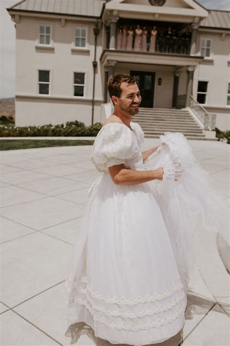 A Man In A White Wedding Dress Is Walking On The Sidewalk Near A Large