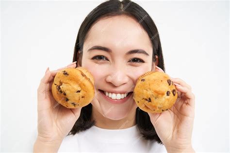 free photo close up portrait of asian woman shows two cupcakes near face and smiles likes