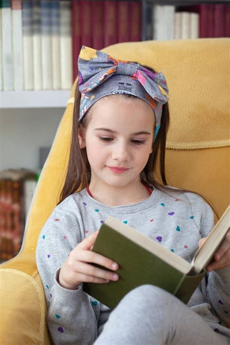 Pretty And Modern School Girl Reading A Book At Home Library Stock