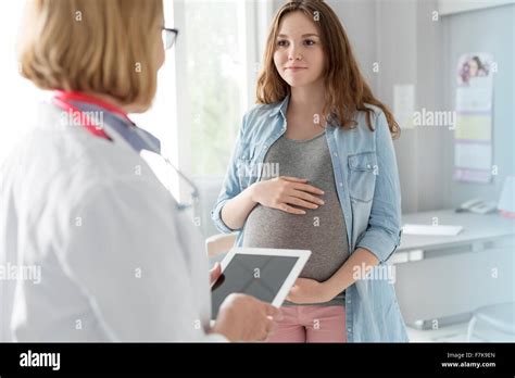 Doctor With Digital Tablet Talking With Pregnant Teenage Patient In