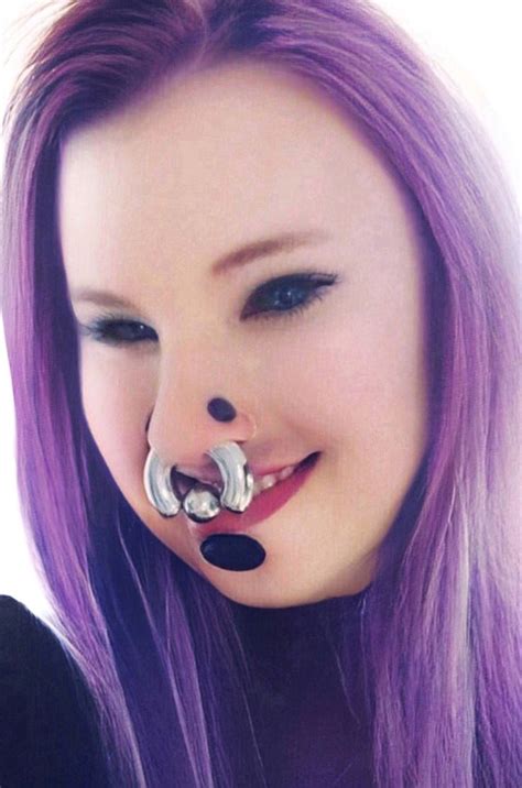 a woman with purple hair wearing a nose ring and piercings on it s nose