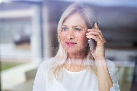 Portrait Of Senior Woman Standing Indoors At Home Using Smartphone
