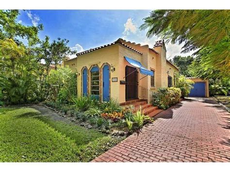 A Yellow House With Blue Shutters In The Front Yard And Trees On Either