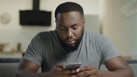 Concentrated Man Sitting With Phone On Couch Portrait Of Black Man