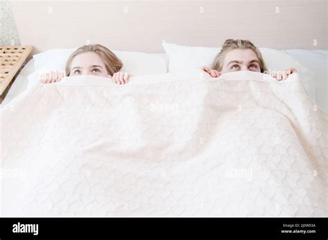 A Young Couple In Bed Covers Half Of Their Faces With A Blanket Hiding