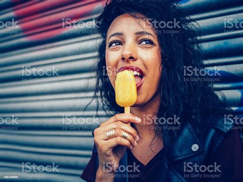 Urban Teen Girl Licking An Orange Colored Flavoured Ice Lolly Stock