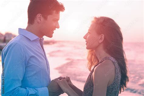 Young Couple Face To Face Holding Hands Each Other Standing On The Beach Shore At Sunset Happy