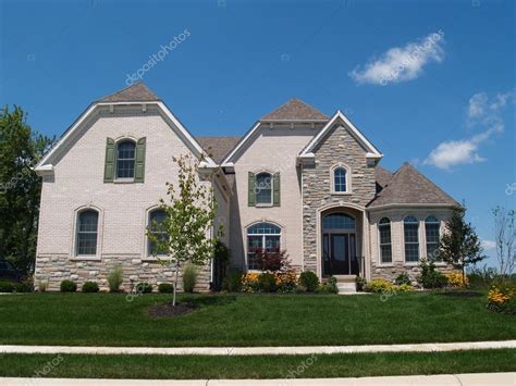 This beautiful traditional 2 story farmhouse features white siding, a front porch with columns, a bottom brick border, pitched roofing, and gable windows. New two story white brick and stone residential home with ...