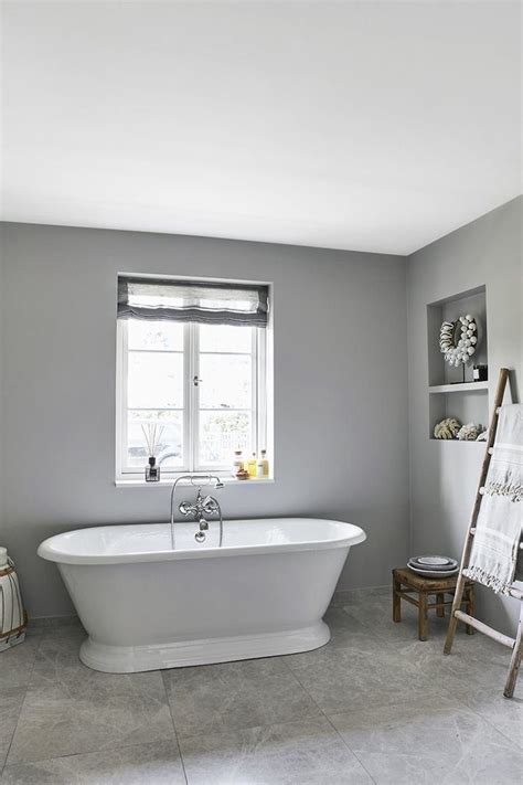 A White Bath Tub Sitting Under A Window Next To A Wooden Stepladder In