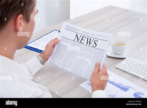 Happy Young Businessman Reading Newspaper At Office Desk Stock Photo