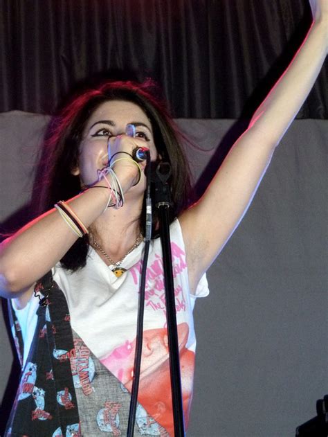 A Woman Singing Into A Microphone While Holding Her Arm Up In The Air With Both Hands