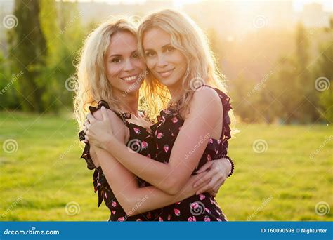 två systrar två vackra blonda glada unga leende kvinnor i den snygga klänningen som kramar i