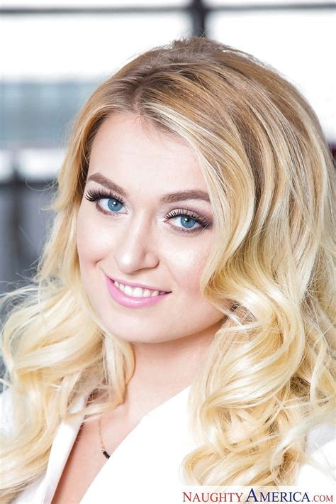 A Woman With Long Blonde Hair And Blue Eyes Smiles At The Camera While Wearing A White Blazer