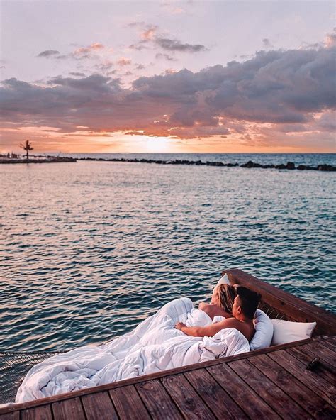 Two People Are Laying On A Boat In The Water At Sunset With One Person Kissing The Other