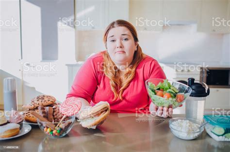 Fat Young Woman In Kitchen Sitting And Eating Food Confused Unhappy