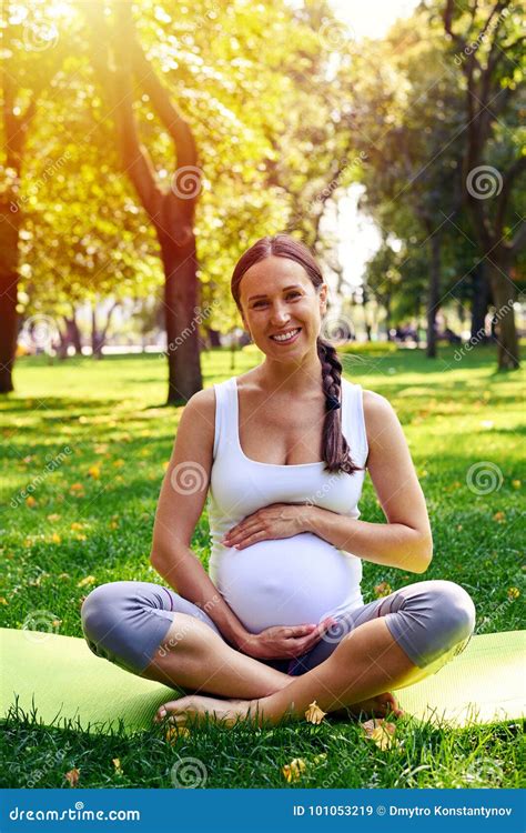 Cheerful Pregnant Woman Holding Belly On Yoga Mat In Park Stock Image