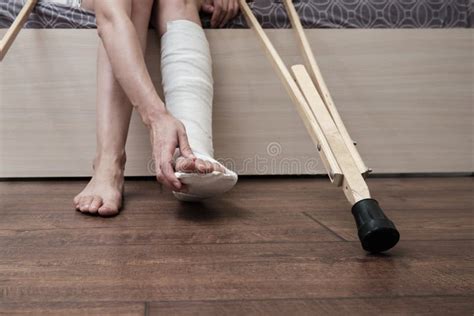 Woman With Broken Leg Sitting On The Bed And Holding Crutches And Touch