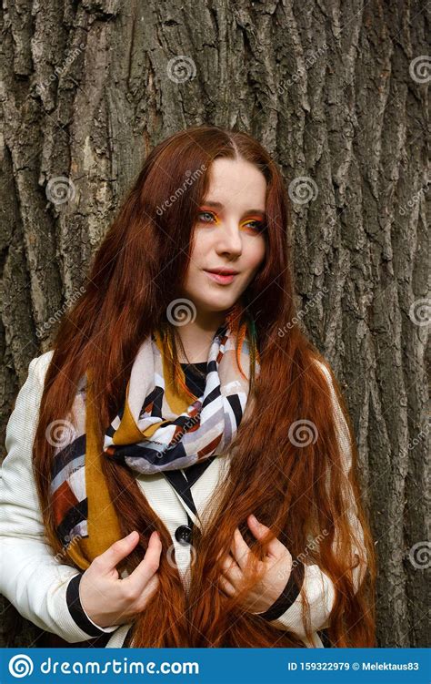Woman With Long Red Hair And Bright Makeup Near A Tree Stock Image