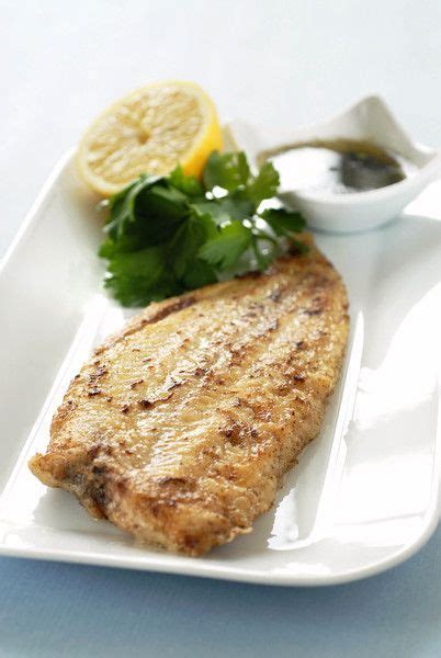 A White Plate Topped With Fish Next To Lemon Wedges And Parsley On Top