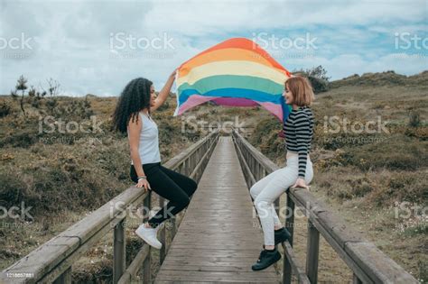 Two Lesbians With The Lgbt Flag On A Bridge Kissing In The Wild Stock