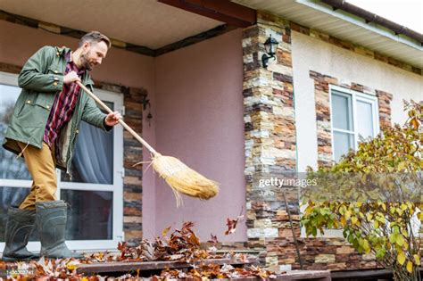 Adult Man Sweeping Leaves From Porch Using Broom High Res Stock Photo