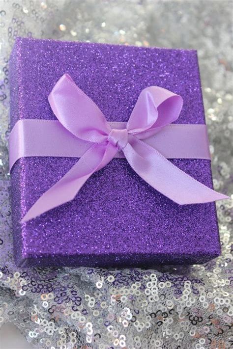 A Purple Gift Box With A Pink Bow On It Sitting On Sequined Fabric