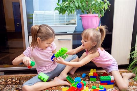 Duas Irmãs Estão Sentadas Em Casa No Chão E Brincando Em Um Conjunto De Construção De Plástico