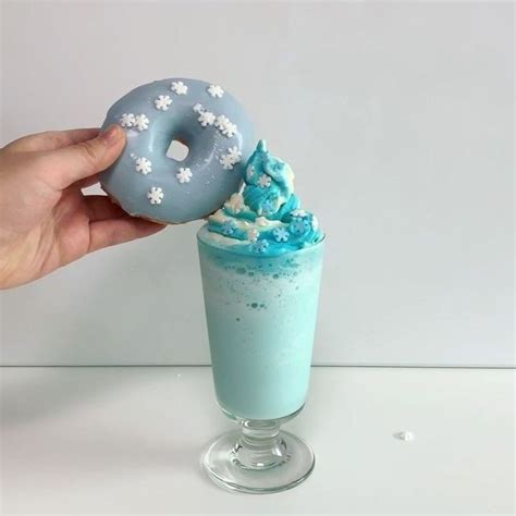 A Hand Holding A Doughnut Over A Drink With Whipped Cream And Sprinkles