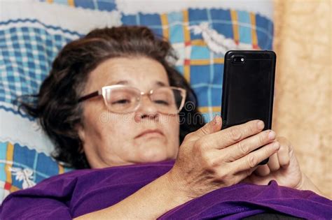 Elderly Woman Lying In Bed During Illness With A Phone In Her Hands